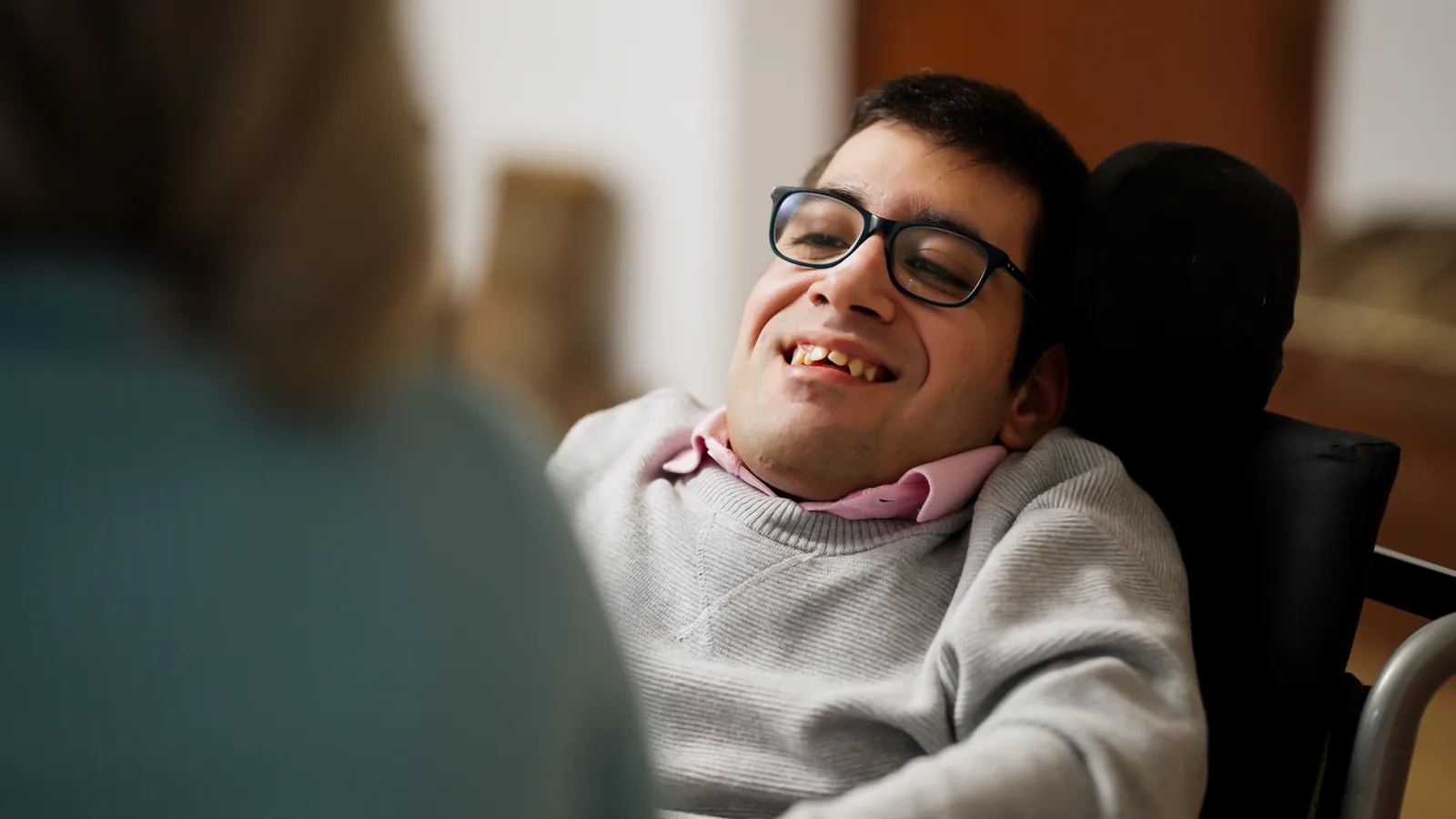 A smiling young man in a wheelchair sharing a laugh with his caregiver at home